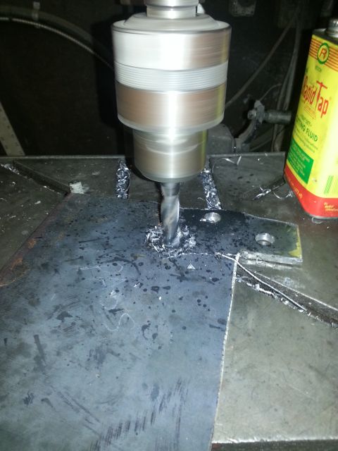 1994 Ford Bronco - A drill press is used to create a hole in a metal plate, with metal shavings accumulating around the drill bit.