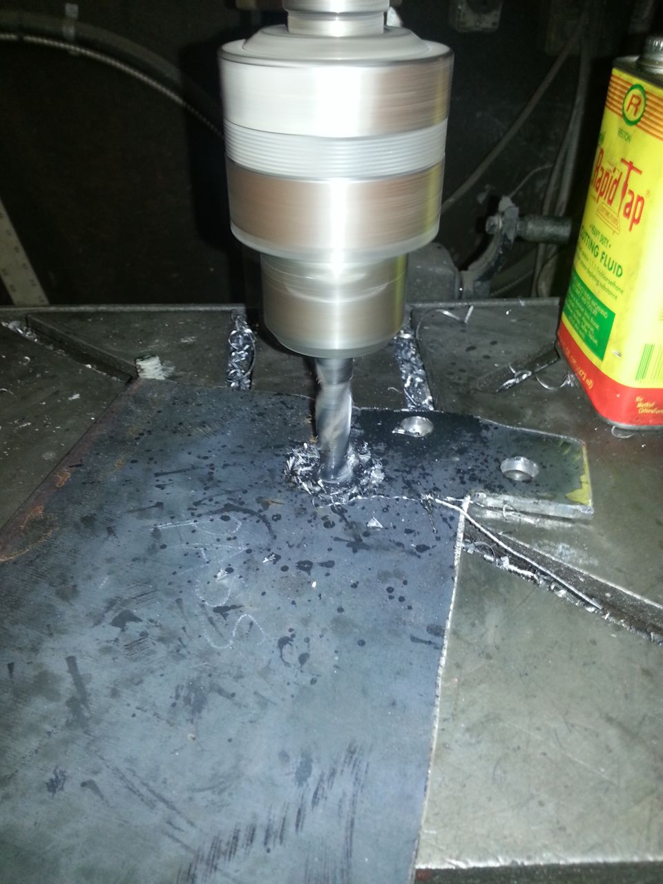 Drill press making a hole in a metal plate, with cutting fluid nearby