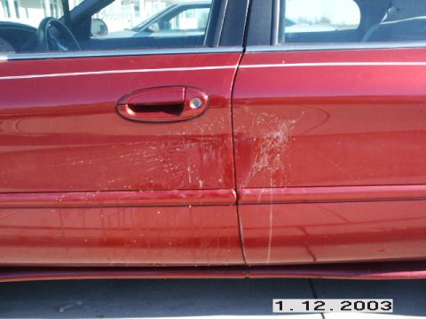 1998 Mercury Sable - Side view of a red car door showing damage from white splatters, with a partial view of another vehicle behind it.