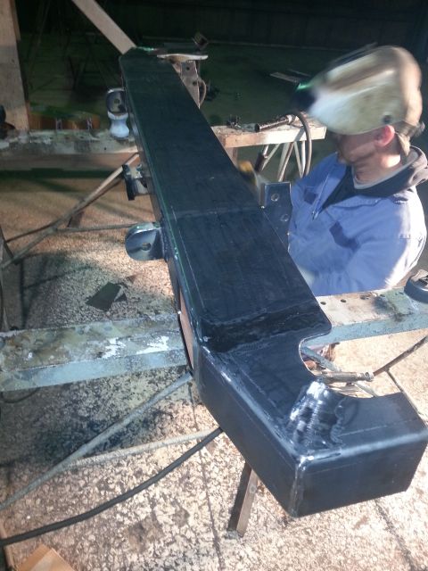 1994 Ford Bronco - A person in a welding mask works on a black bumper supported by sawhorses.