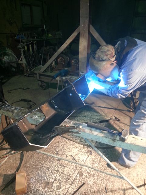 1994 Ford Bronco - Man welding a metal component in a cluttered garage setting.