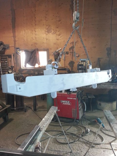 1994 Ford Bronco - A vehicle frame is suspended by chains and being prepped for paint in a workshop setting.