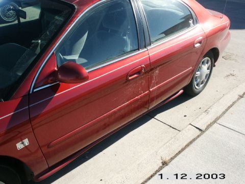 1998 Mercury Sable - A red sedan is parked on a concrete surface, showing its side profile and a portion of the interior.