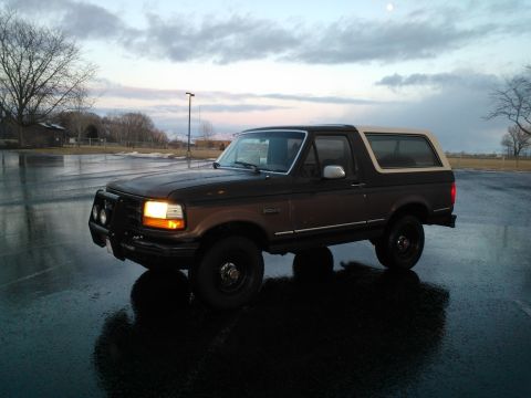 1992 Ford Bronco - A two-tone Ford Bronco sits in a wet parking lot under a cloudy sky.