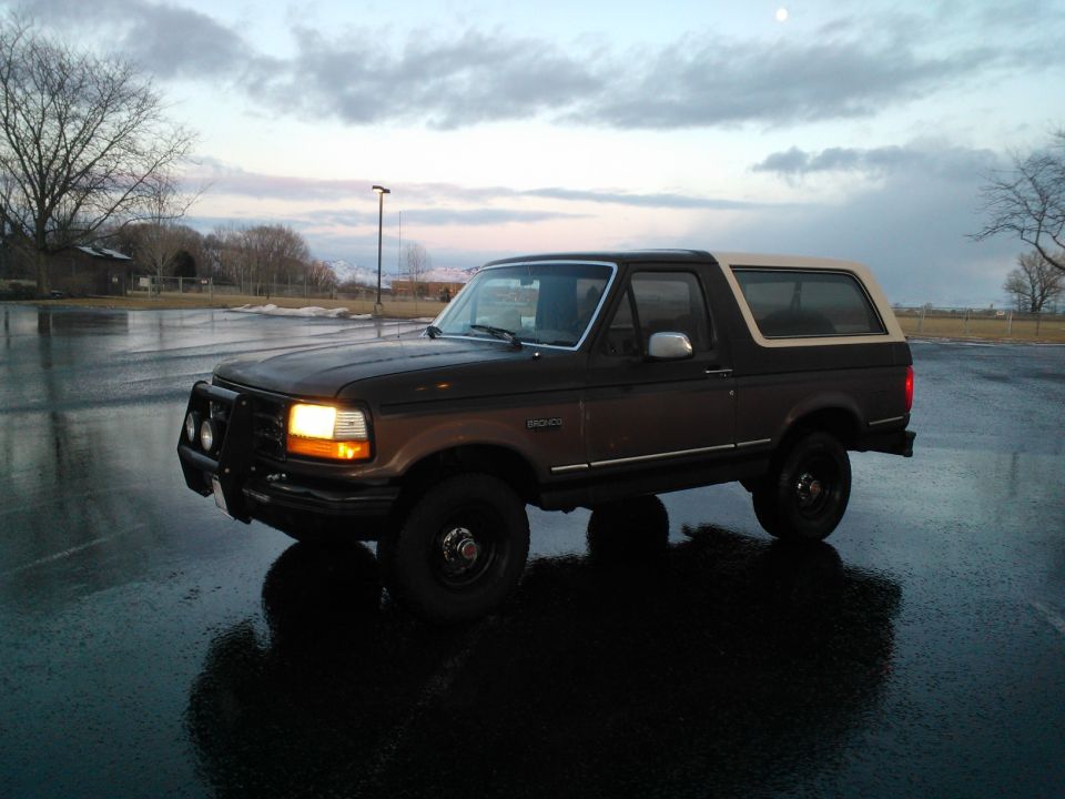 Dark brown and tan Ford Bronco parked on a wet asphalt lot