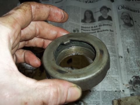1990 Ford Bronco - A close-up of a greasy wheel bearing lock nut is held in a hand, with a newspaper visible in the background.