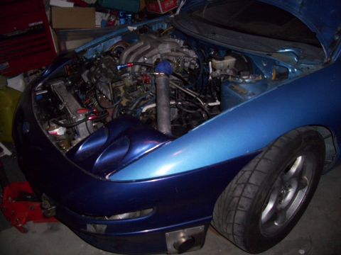 1995 Ford Probe - The engine bay of a blue car is visible with the hood open, revealing the engine and front fender details.