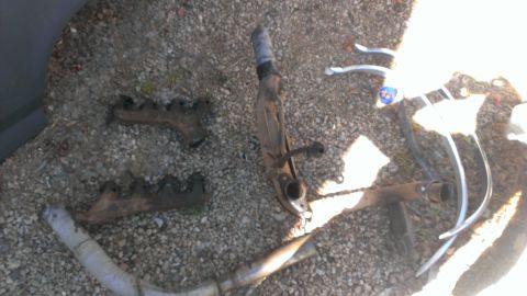 1990 Ford Bronco - Various exhaust manifold and suspension components are laid out on a gravel surface.