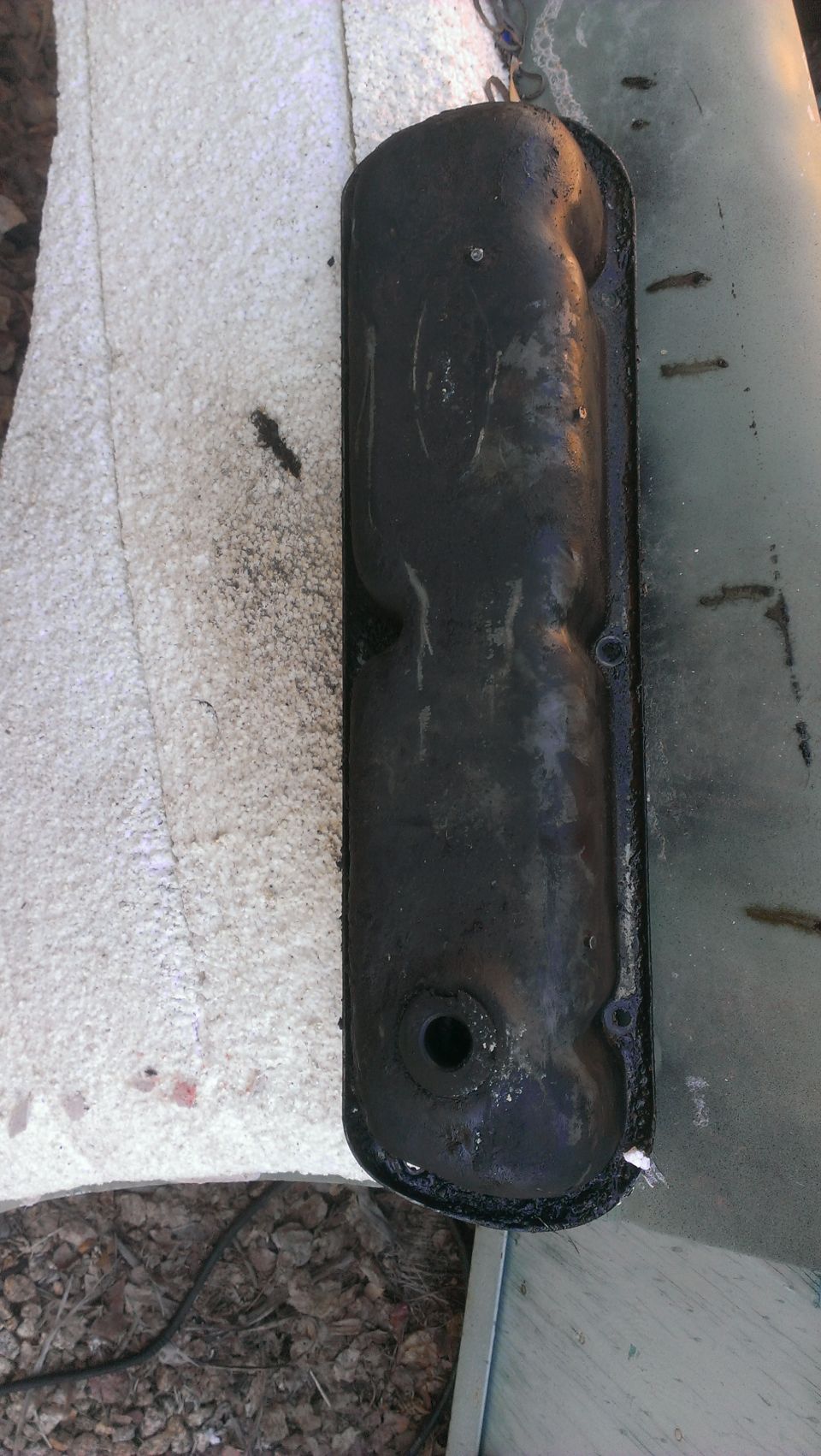 Black valve cover with oil residue, on a white cloth and metal surface