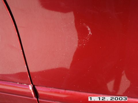 1998 Mercury Sable - Close-up view of a red car's door seam, showing some minor paint damage and reflections.