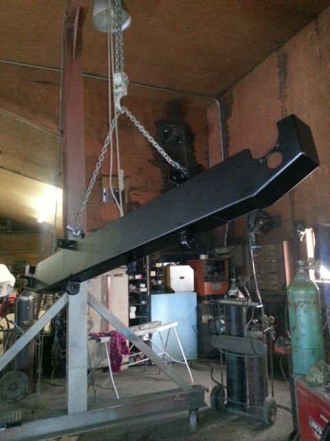 1994 Ford Bronco - A metal beam is suspended by a chain hoist in a workshop setting with various tools and equipment visible.
