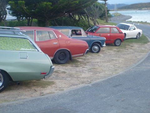 1969 Lincoln Continental - A collection of vintage cars are parked in a row on a dirt lot next to a body of water.