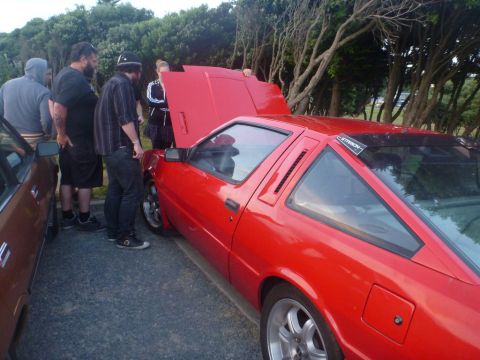 1969 Lincoln Continental - Several people examine a red sports car with its hood open.
