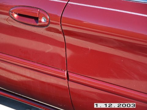 1998 Mercury Sable - Close-up of a red car's side panel, revealing minor imperfections and a door handle with a keyhole.