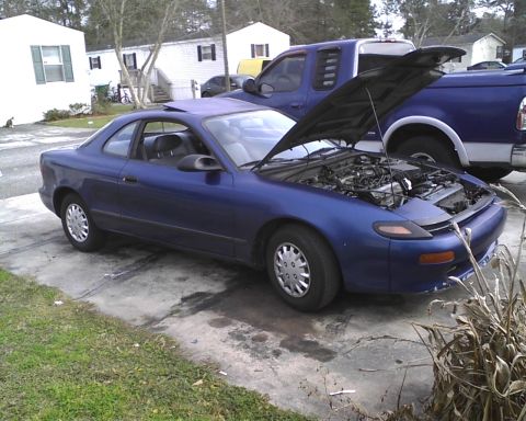 1991 Toyota Celica - A blue 1991 Toyota Celica coupe is parked outside with its hood open, next to a blue pickup truck.