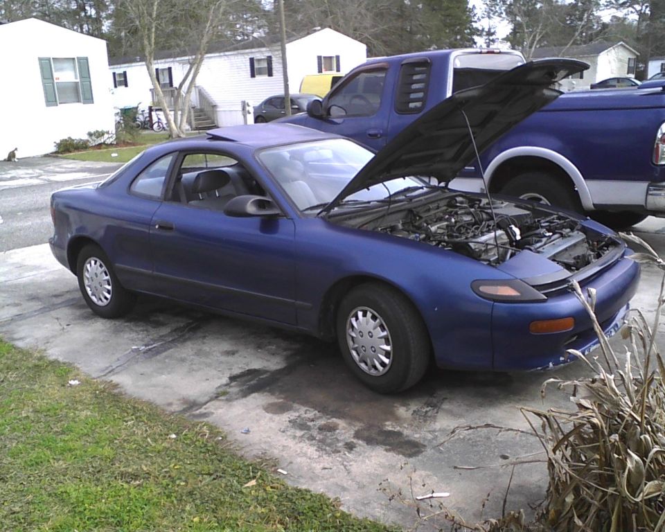 Blue 1991 Toyota Celica coupe parked next to a blue pickup truck, hood of Celica is open