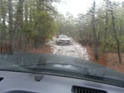 1987 Toyota 4Runner - Two white SUVs navigate a wet and muddy path through a wooded area, viewed from inside a vehicle.