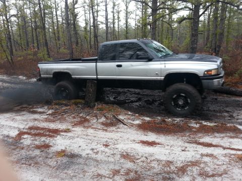 1987 Toyota 4Runner - A lifted Dodge Ram pickup truck is stuck in the mud, with smoke billowing from its tires in a forest setting.
