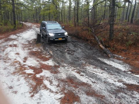 1987 Toyota 4Runner - A dark SUV is stuck in the mud on a dirt road in a forest.