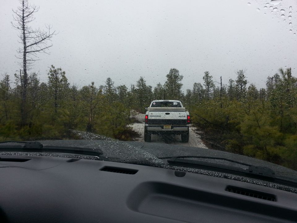 White Dodge pickup truck with 4x4 badge driving on a dirt road in a wooded area