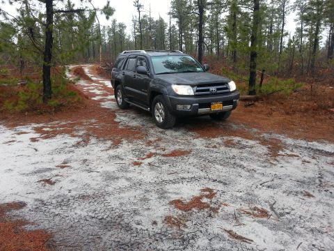 1987 Toyota 4Runner - Dark SUV parked on a sandy, pine-needle-covered road within a wooded area.