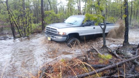 1987 Toyota 4Runner - A silver pickup truck navigates through a flooded wooded area, kicking up water as it goes.
