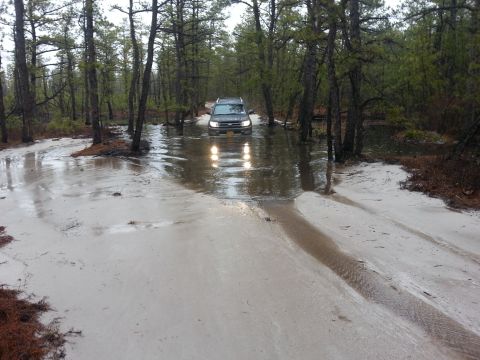 1987 Toyota 4Runner - SUV navigates a waterlogged path in a wooded area, with visible "SUPERMOTORS" branding at the bottom right.
