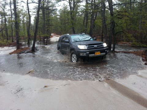 1987 Toyota 4Runner - SUV navigates a flooded path in a wooded area, kicking up water.