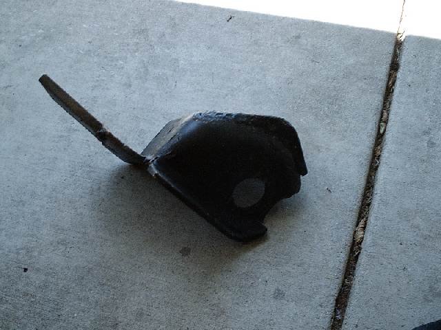 Black metal bracket with round hole and long bent tab lying on concrete
