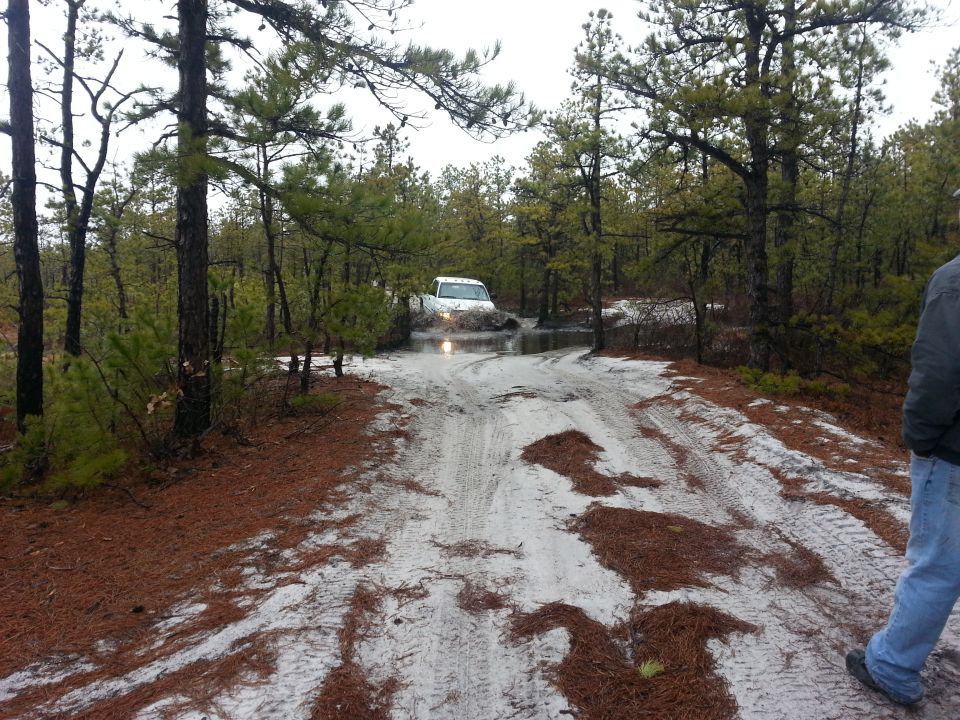 1987 Toyota 4Runner driving through mud on a dirt road in a wooded area