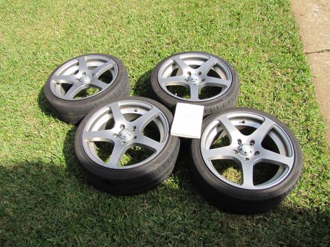 1995 Ford Bronco - Four alloy wheels and tires are laid out on a grassy lawn next to a concrete path.