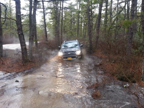 1987 Toyota 4Runner - A Toyota 4Runner navigates a flooded path in a wooded area, kicking up water and mist.