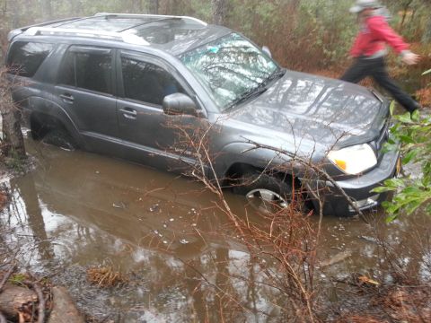 1987 Toyota 4Runner - A gray SUV is stuck in a muddy, water-filled area with a person walking in the background.