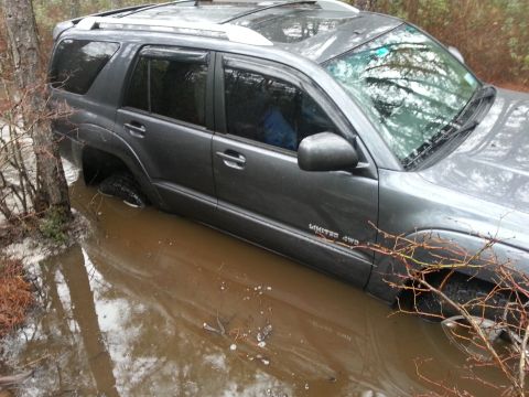 1987 Toyota 4Runner - This SUV is partially submerged in muddy water, with branches encroaching on its side.
