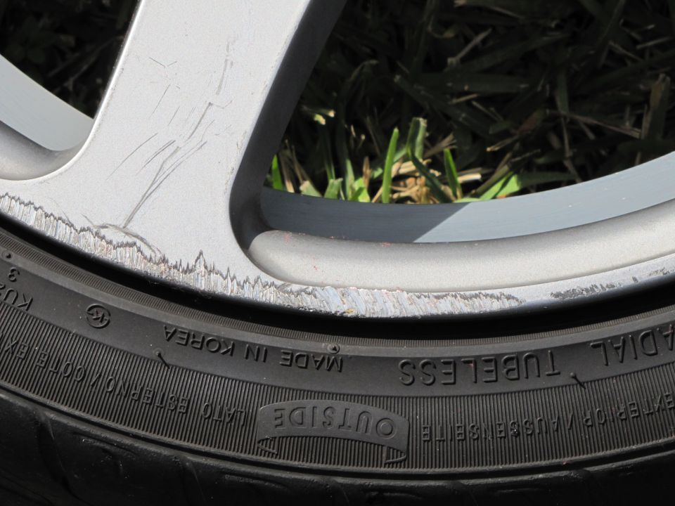 Scratched silver alloy wheel with curb rash next to a black tire with "MADE IN KOREA" visible