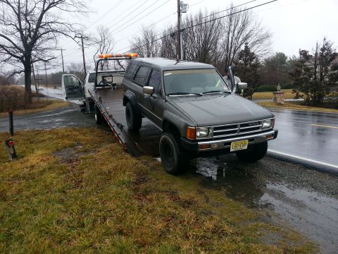 1987 Toyota 4Runner - A gray 1987 Toyota 4Runner is loaded onto a tow truck on a wet day.