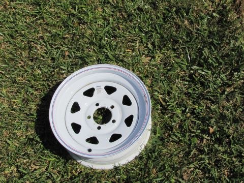 1995 Ford Bronco - A single white steel wheel with red and blue pinstripes lies on a grassy surface.