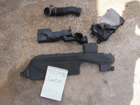 1995 Ford Bronco - Several black plastic air intake components are laid out on a concrete surface, alongside a notepad with handwritten text.