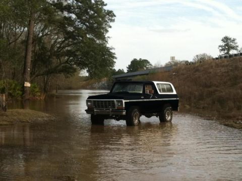 1994 Ford Bronco - A black SUV navigates through a flooded area, its front grille and headlights clearly visible.