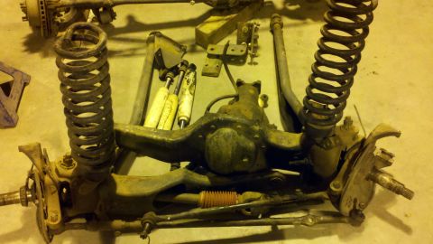 1996 Ford Bronco - Disassembled front axle and suspension parts, including coil springs and shock absorbers, laid out on the floor.