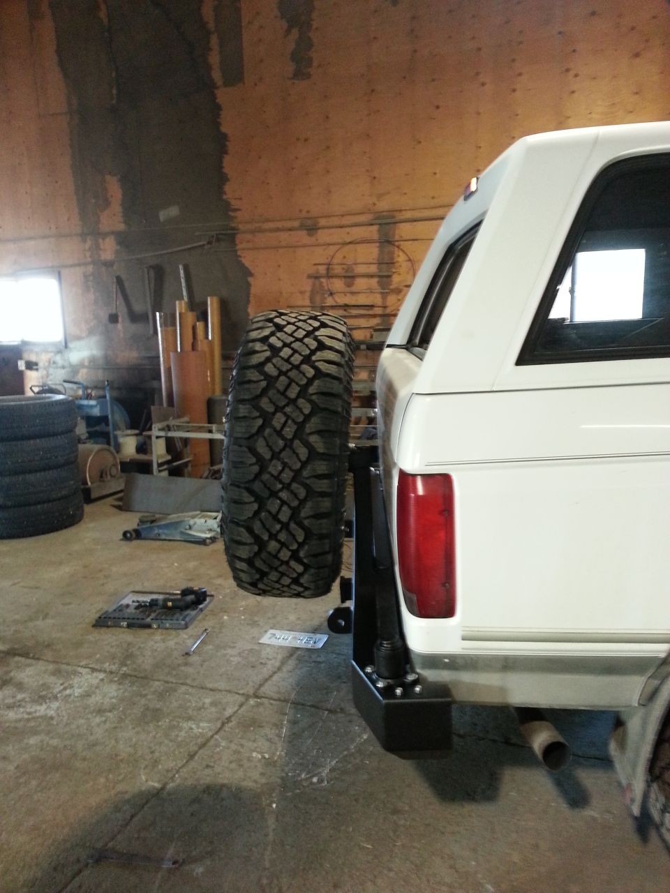 White SUV's rear with spare tire carrier and large off-road tire. Appears to be a 1992 Ford Bronco