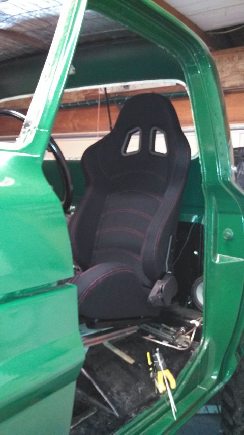 1967 Ford F-250 - Interior view of a green truck, a black racing seat with red stitching and a visible steering wheel.