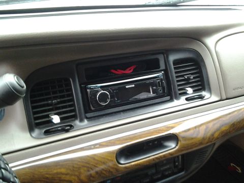 1998 Mercury Grand Marquis - The interior of a vehicle shows a Kenwood stereo installed in the dashboard, surrounded by air vents and wood grain trim.