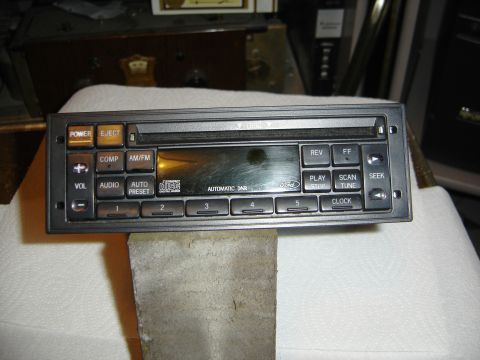 1996 Ford Bronco - A factory Ford AM/FM cassette-style head unit removed from the dash and stood on a white cloth-covered bench, its faceplate showing POWER,…