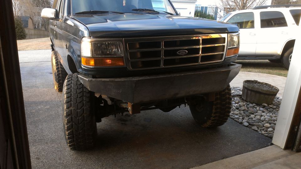 Dark green Ford Bronco with aftermarket bumper and large tires, front view