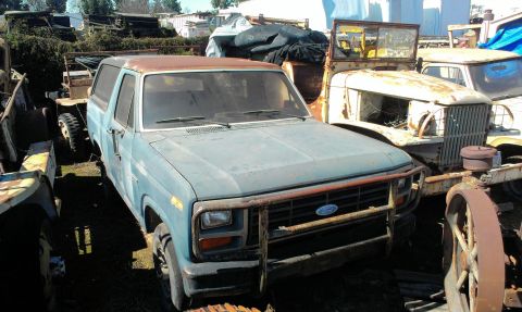 1994 Ford Bronco - Junkyard scene with a blue Ford Bronco and other old vehicles under a clear sky.