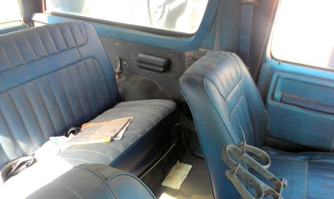 1994 Ford Bronco - The interior of an older blue SUV shows worn vinyl seats and door panels, with a magazine resting on the back seat.