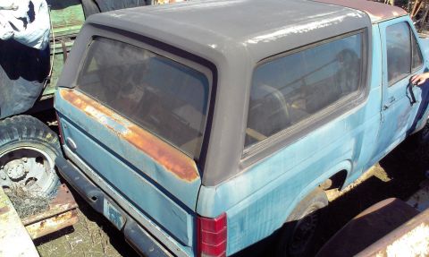 1994 Ford Bronco - A blue Ford Bronco with a black top shows significant rust damage on its rear quarter panel.