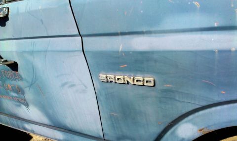 1994 Ford Bronco - Close-up of a blue Ford Bronco's side panel, showing the 'BRONCO' emblem and some faded text on the door.