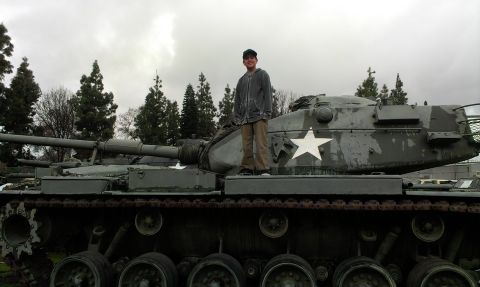 1994 Ford Bronco - A person stands atop a military tank, which is painted in camouflage colors and features a prominent white star.